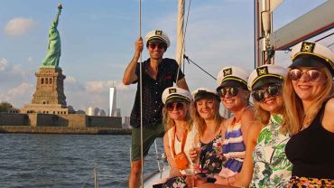 On the cabin top of sailboat posing for photos with the Statue Of Liberty