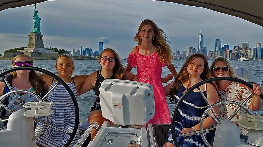 girls at the helm of a sailboat at the Statue Of Liberty