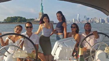 At the helm of a sailboat posing for photos with the Statue Of Liberty