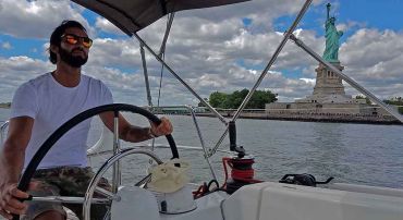 Male sailing at the helm near the Statue Of Liberty